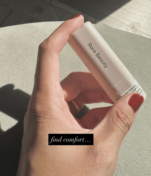 Selena Gomez's hand with a burnt orange manicure holding a lip butter lab sample